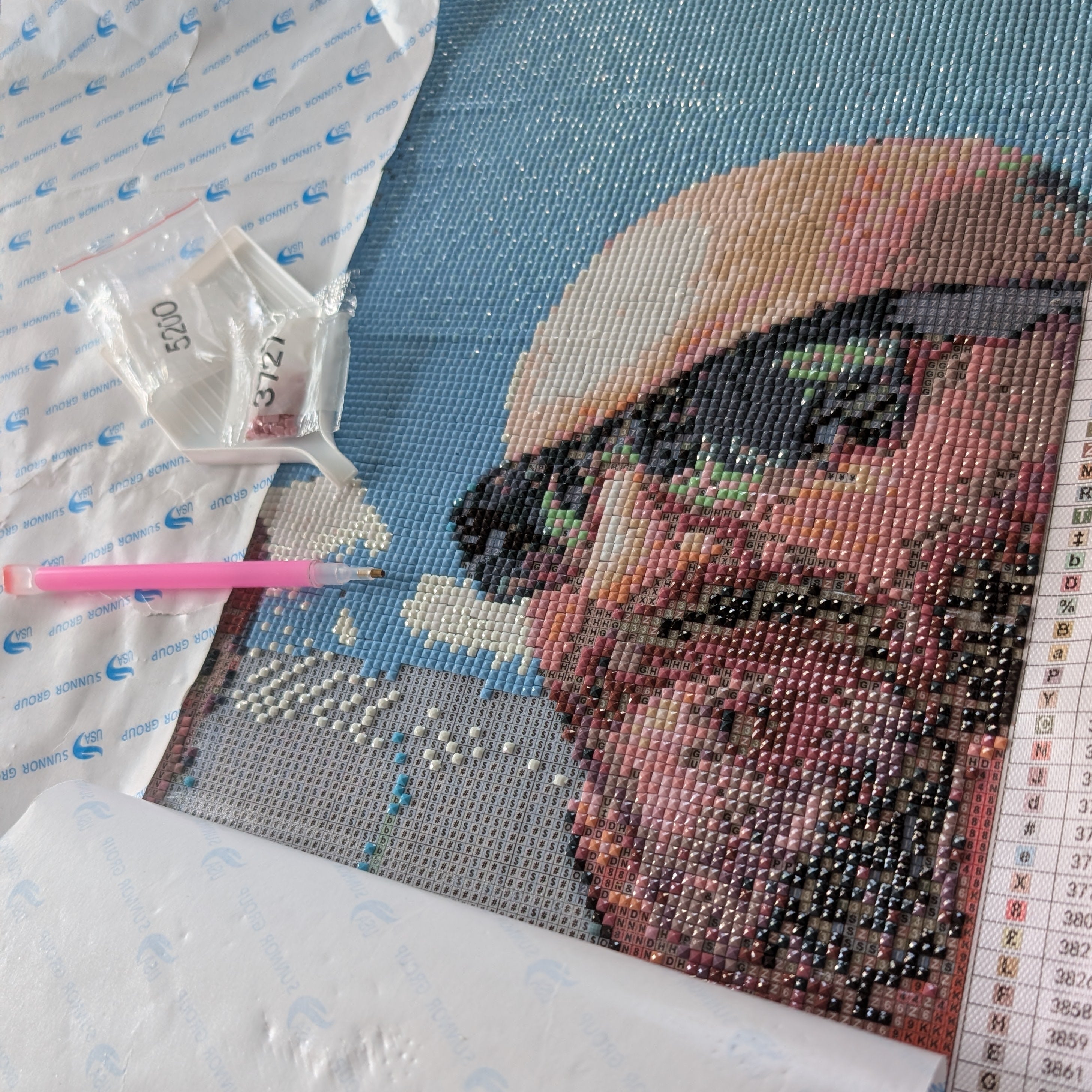 Toile de diamond painting personnalisée en cours de montage : portrait en diamants carrés, stylo applicateur et sachets de diamants numérotés